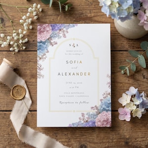 May include: A wedding invitation with floral accents. The invitation features the names "SOFIA" and "ALEXANDER" in gold lettering, along with the wedding date and location. The design includes blue, purple, and pink flowers.