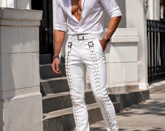 May include: A white long-sleeved button-down shirt paired with white trousers featuring vertical lace-up detailing along the outer legs, silver-toned metal buckles at the waist, and a matching white belt, complemented by white leather boots.