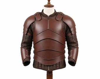 May include: A brown leather chest and shoulder armor set featuring layered plates, worn over a dark brown quilted long-sleeve garment. The armor includes articulated shoulder pauldrons and forearm guards, secured with straps and metal rivets.