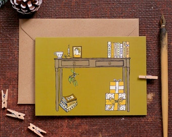 May include: A green card with a brown wooden desk with a drawer, a small picture frame, a cup, a candle, a stack of books, a mistletoe sprig, and wrapped gifts. The books have titles like "Emma", "Pride & Prejudice", and "Sense & Sensibility".