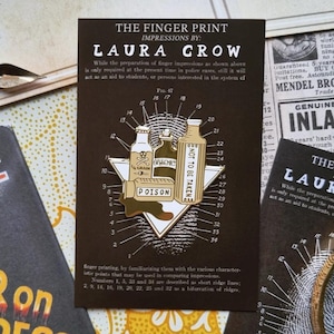 May include: A dark brown enamel pin with a poison bottle design, featuring the text "POISON" and "NOT TO BE TAKEN". The pin, part of a Laura Grow collection, has a vintage aesthetic. It's displayed with related vintage ephemera.