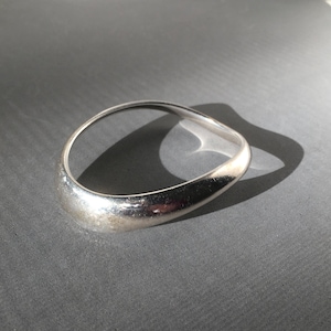 May include: A silver bangle bracelet with a smooth, curved design. The bracelet is made of metal and has a polished finish.