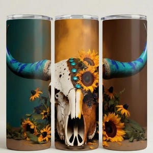 May include: Tumblers featuring a detailed illustration of a cow skull adorned with sunflowers and turquoise accents. The horns are painted blue. The background colors vary from teal to brown, creating a striking contrast.
