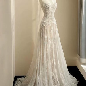 Peut inclure: Robe de mari&eacute;e blanche sur mannequin. La robe pr&eacute;sente un d&eacute;collet&eacute; en c&oelig;ur et est orn&eacute;e de dentelle complexe sur le corsage et la jupe. La jupe descend jusqu'au sol, cr&eacute;ant une silhouette romantique et &eacute;l&eacute;gante. Un voile transparent est drap&eacute; sur la t&ecirc;te du mannequin.