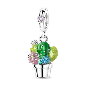 May include: A silver charm with a cactus design. The charm features a green cactus with pink and blue flowers in a silver pot. A small pink flower is at the top of the charm. The charm is designed to be attached to a bracelet or necklace.