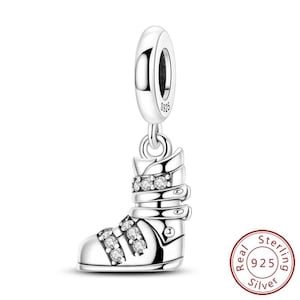 May include: A silver charm in the shape of a ski boot, adorned with clear crystals. The charm is suspended from a loop, and a small tag reads "S925". A circular stamp indicates "Real Sterling 925 Silver".