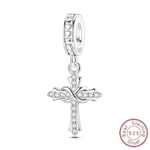 May include: A silver charm with a cross pendant. The cross is adorned with clear gemstones and an infinity symbol. The top of the charm has a ring with heart-shaped cutouts. The charm is marked with "S925" and "Real Sterling Silver".