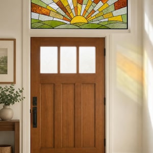 May include: A rectangular stained glass transom window featuring a sunrise motif with yellow, orange, and green glass segments. The design depicts a sun rising over rolling hills, installed above a wooden door with three glass panes.