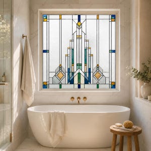Op de afbeelding: Een vierkant raam met een geometrisch glas-in-loodontwerp met heldere, witte, blauwgroene, blauwe en amberkleurige glaspanelen in een symmetrisch, verticaal patroon met een dun metalen frame, geplaatst boven een vrijstaand bad.