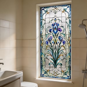 May include: A stained glass window featuring a floral design with blue and purple irises. The window is framed in a blue border and is installed in a bathroom setting. The window is rectangular.