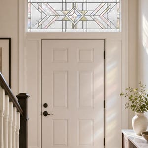 May include: A white six-panel door with a rectangular transom window above it. The transom features a geometric leaded glass design with clear, textured, and iridescent glass panes arranged in a symmetrical pattern with a central diamond.