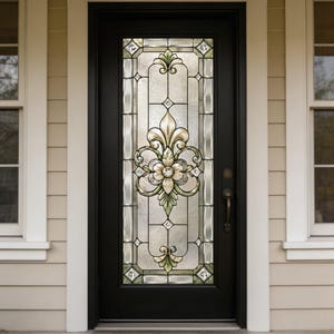 Könnte beinhalten: Schwarze Haustür mit dekorativer Glasscheibe. Das Glas weist ein florales Design mit goldenen, grünen und transparenten Akzenten auf. Die Tür hat einen Griff und ist in einer beigefarbenen Außenwand mit weißer Verkleidung eingesetzt.