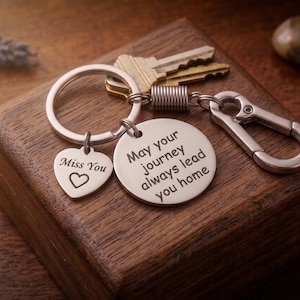 Può includere: Un portachiavi argentato con due ciondoli. Un ciondolo a forma di cuore con le parole "Miss You" e un simbolo di cuore. L'altro ciondolo rotondo dice "May your journey always lead you home". Il portachiavi ha anche un moschettone e un anello con chiavi.