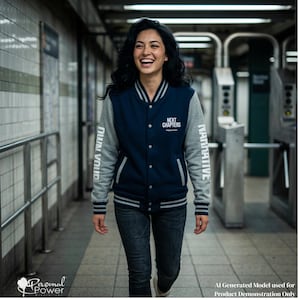 May include: A navy blue and heather gray varsity jacket featuring a button-up front, striped ribbed cuffs, and collar. The chest displays the text NEXT CHAPTERS, while the sleeves feature the vertical text OWN YOUR NARRATIVE in white.