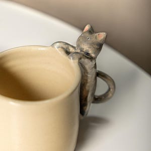 Caneca artesanal com estampa de gato: xícara de café de cerâmica com alça e borda em formato de gatinho microesculpido.