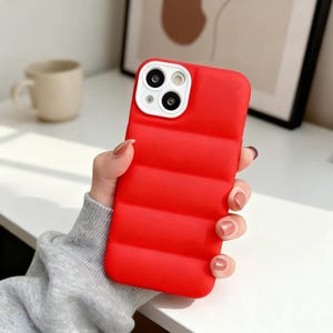 Könnte beinhalten: Eine leuchtend rote Handyhülle mit Steppmuster. Die Hülle hat ein weißes Kameramodul. Die Hülle soll das Telefon vor Beschädigungen schützen.