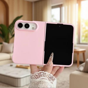 Puede incluir: Una funda para smartphone plegable de color rosa claro con acabado mate, que presenta un recorte rectangular para un sistema de doble cámara y un flash. La funda está diseñada para un dispositivo con pantalla plegable, mostrando una pantalla negra.