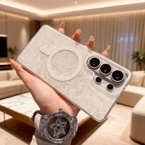 Puede incluir: Una funda transparente para teléfono con un diseño veteado blanco nacarado. La funda tiene un accesorio magnético circular blanco y un módulo de cámara con tres lentes. Se ve un reloj de lujo con una correa de cuero blanca.