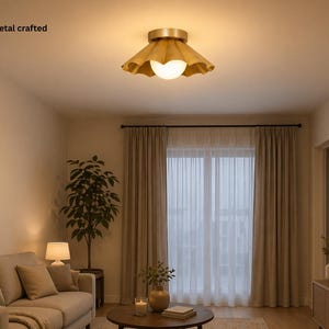 May include: A ceiling light fixture with a gold-colored metal base and a wooden shade. The shade has a ruffled design and surrounds a white, spherical light. The text "wood metal crafted" is visible.
