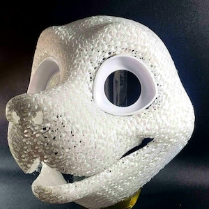 Op de afbeelding: Een witte, 3D-geprinte dierenmasker met grote oogopeningen en een gestructureerd oppervlak. Het masker heeft een snuit en is ontworpen om te worden gedragen. Het masker is gemaakt van een poreus materiaal.