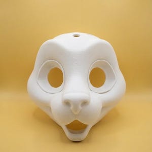 Könnte beinhalten: Eine weiße, 3D-gedruckte Tiermaskenbasis mit großen, kreisförmigen Augenhöhlen, einer ausgeprägten Schnauze und einem offenen Mund. Die Oberfläche weist eine feine, geschichtete Textur auf, die für die additive Fertigung typisch ist, mit einem kleinen Loch oben.