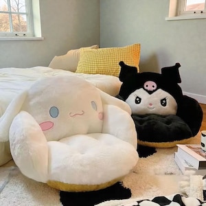 Peut inclure: Deux fauteuils en peluche représentant des personnages de dessins animés. L'un est blanc avec des accents bleus et roses, l'autre est noir avec un crâne et des accents roses. Les deux chaises sont sur un tapis.
