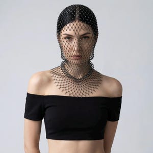 Op de afbeelding: Een zwarte, met kralen bezette hoofdbedekking en gezichtssluier met een netachtig ontwerp. De sluier reikt tot aan de schouders en creëert een uniek, elegant accessoire. De hoofdbekleding is versierd met kleine, sprankelende versieringen.