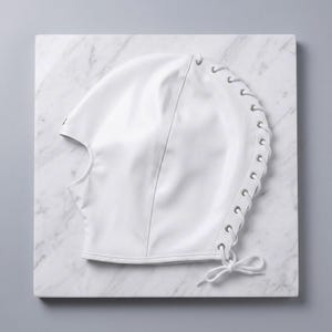 Puede incluir: Una capucha blanca con una abertura para la cara y un cierre de cordones en el lateral. La capucha est&aacute; hecha de un material liso y brillante y est&aacute; atada con un lazo. La capucha est&aacute; sobre una superficie de m&aacute;rmol blanco.