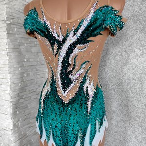 May include: A teal and nude-coloured leotard with a decorative design. The leotard features a teal bodice with white accents and is embellished with sparkling rhinestones. The design extends up the back and over the shoulders.