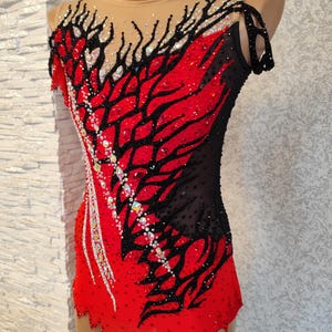 May include: A red and black leotard with an eye-catching design. The garment has a red base with black patterns and is embellished with sparkling details. It features a sheer neckline, making it suitable for gymnastics or dance performances.