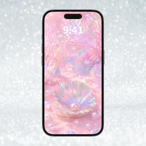 Peut inclure: Un smartphone au cadre noir affichant un fond d'écran numérique représentant un coquillage irisé scintillant contenant une perle sur un sable rose, entouré de structures coralliennes et de bulles flottantes, avec l'heure 9:41 affichée.