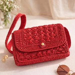 Peut inclure: Un sac à bandoulière rouge tissé avec une fermeture à rabat et un bouton doré. Le sac a une bandoulière tissée et un motif texturé. Le sac mesure environ 23 cm de large et 15 cm de haut.