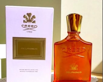 May include: A Creed Delphinus perfume bottle with orange glass and a gold cap, accompanied by its white rectangular box. The box features the Creed logo, the text Delphinus, and House Established 1760. The bottle contains 100 ml or 3.3 fl oz.