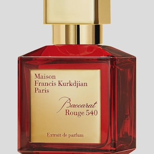 May include: A red perfume bottle with a gold cap. The bottle has a rectangular shape with beveled edges. The label reads "Maison Francis Kurkdjian Paris Baccarat Rouge 540 Extrait de parfum."