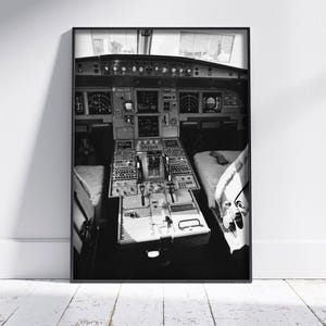 May include: A black and white framed wall art print depicting the interior cockpit of an airplane. The view shows the central pedestal, throttle levers, overhead panels, and flight instrument displays, all captured in a high-contrast monochrome style.