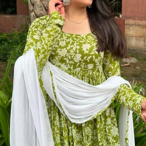 Puede incluir: Un vestido verde de manga larga con un estampado floral blanco y una bufanda blanca a juego. El vestido tiene un cuello redondo y una falda fluida. La bufanda est&aacute; drapeada sobre los hombros. Adecuado para ocasiones informales o semiformales.