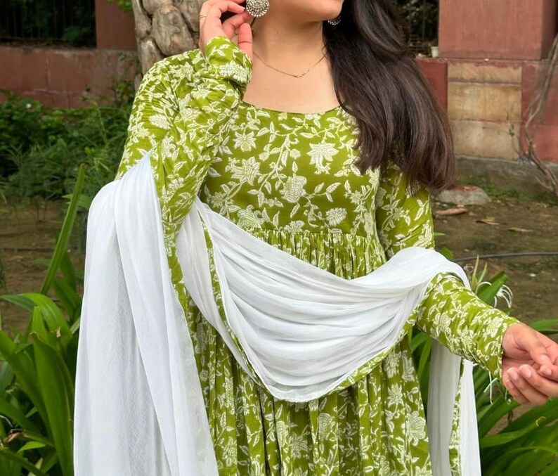 Puede incluir: Un vestido verde de manga larga con un estampado floral blanco y una bufanda blanca a juego. El vestido tiene un cuello redondo y una falda fluida. La bufanda est&aacute; drapeada sobre los hombros. Adecuado para ocasiones informales o semiformales.