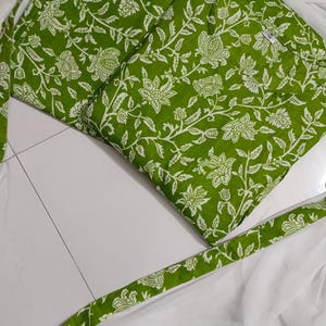 Puede incluir: Tela verde con un estampado floral blanco, doblada y dispuesta con tela blanca y ribete a juego con estampado verde. La tela es probablemente para ropa o decoraci&oacute;n del hogar.