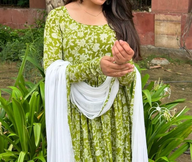 Puede incluir: Un vestido verde de manga larga con un estampado floral blanco y una bufanda blanca a juego. El vestido tiene un cuello redondo y est&aacute; hecho de una tela ligera. La bufanda est&aacute; drapeada sobre los hombros.