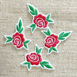 May include: Four embroidered iron-on patches, each featuring a single red rose blossom with green leaves. The rose petals are stitched in vibrant red thread, while the leaves are detailed in bright green, all outlined with a white border.