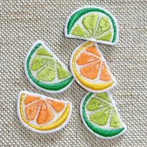 May include: Five embroidered patches shaped like citrus fruit wedges. Three patches feature light green and dark green lime segments, while two patches display bright orange and yellow lemon or orange segments, all with white stitched borders.