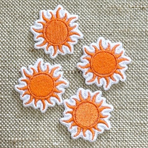May include: Four embroidered sun patches featuring a bright orange circular centre with radiating orange flames surrounded by a white stitched border. Each patch displays a consistent sun design with detailed thread work and a clean edge finish.