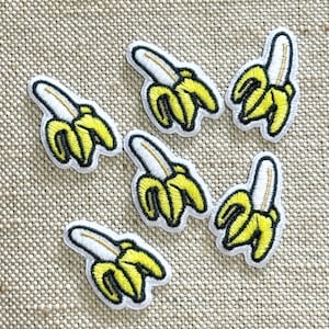 Puede incluir: Seis parches bordados, cada uno con un diseño de una pequeña banana pelada. Las bananas son de color amarillo brillante con centros blancos y están delineadas con hilo negro. Cada parche tiene un borde blanco, creando una apariencia uniforme.
