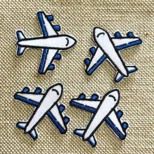 Op de afbeelding: Vier geborduurde patches in de vorm van vliegtuigen, elk met een witte romp, blauwe accenten op de vleugels en zwarte omlijningen. De patches zijn in een raster geplaatst en tonen een consistent ontwerp van een verkeersvliegtuig.