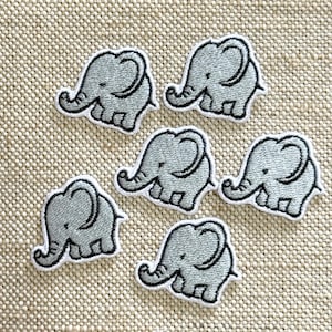 Op de afbeelding: Een set van zes geborduurde patches, elk met een lichtgrijze olifant met een donkergrijze omlijning. De olifanten zijn afgebeeld in zijaanzicht met een slurf, een groot oor en vier poten, gerangschikt in een verspreid patroon op een textuurrijke stof.
