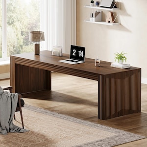 May include: A dark brown wooden desk with a laptop displaying "2 14" on the screen. A desk lamp, a small plant, and a glass of water are on the desk. The desk is in a well-lit room with a window and a patterned rug.