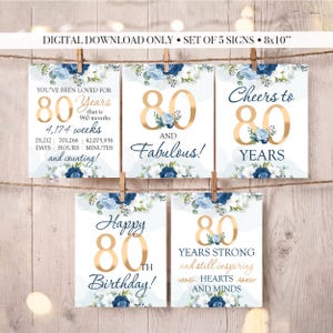 May include: A set of five 8x10 inch digital signs for an 80th birthday celebration. Each sign features gold text, navy blue accents, and floral illustrations in shades of blue and white. The text includes phrases like 80 and Fabulous and Cheers to 80 Years.