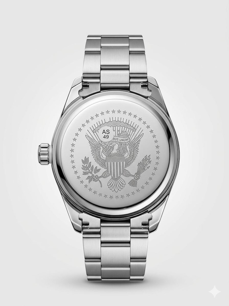 Op de afbeelding: Roestvrijstalen polshorloge met zilveren band. De wijzerplaat van het horloge heeft een gedetailleerde gravure van de Amerikaanse adelaar en de woorden "E Pluribus Unum". Het horloge heeft een ronde wijzerplaat en een zilveren kroon.