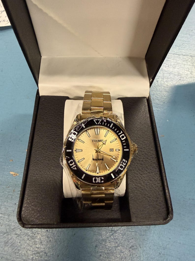 Pu&ograve; includere: Orologio da polso color oro con lunetta nera, presentato in una scatola nera. Il quadrante dell'orologio &egrave; dorato con la scritta "TRUMP" in alto. L'orologio ha un cinturino dorato ed &egrave; nuovo nella sua confezione.