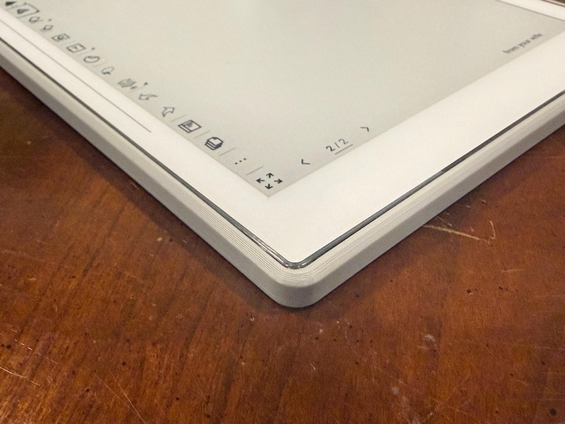 May include: A white digital tablet with a gray frame, viewed at an angle. The screen is bright and clean, with icons and navigation controls visible. The device rests on a wooden surface, highlighting its modern aesthetic.